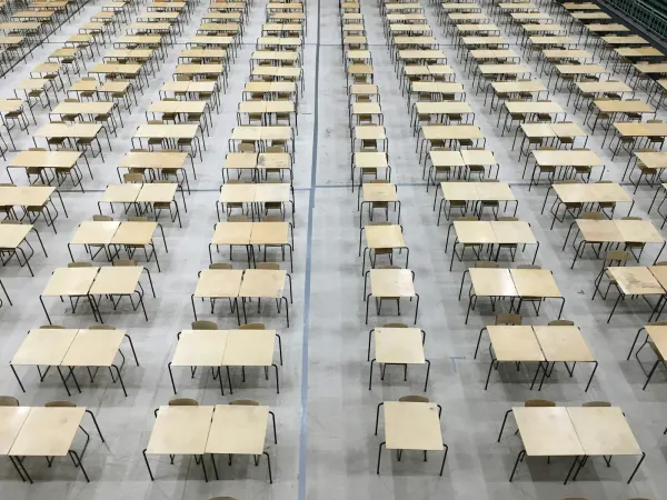 Rows of single desks set out in an exam hall.