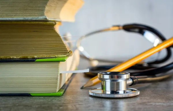 A stethoscope and pencil resting on a stack of textbooks.