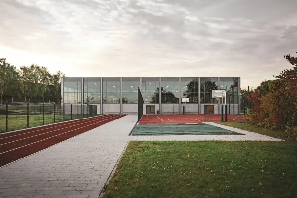 A modern school campus with a running track, sports court and glass sports hall.
